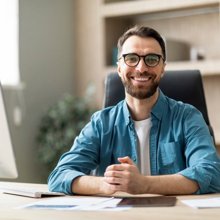 Hombre sonriente con gafas sentado en el escritorio de la oficina.